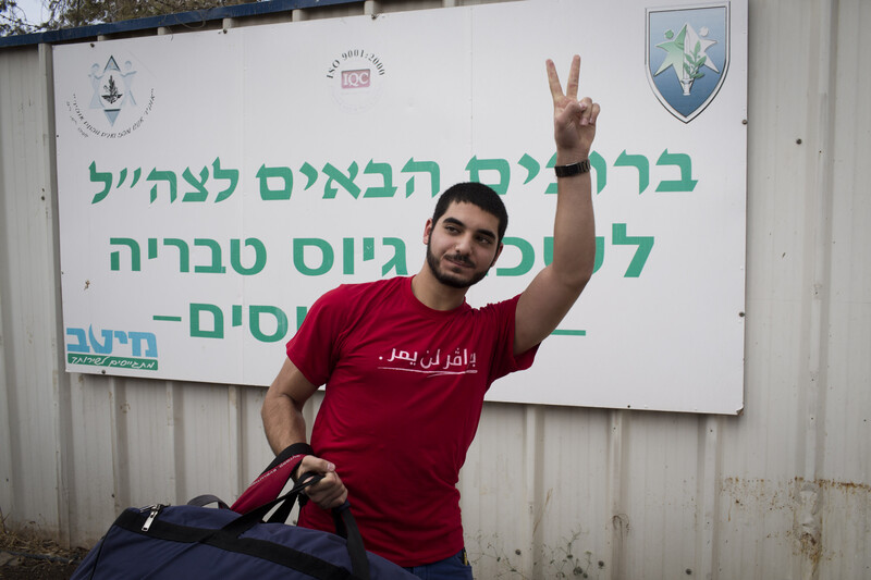 Young man gives carrying duffel bag gives victory gesture with his hand