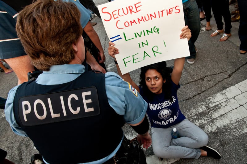 Young woman holding sign sits in street facing police officer