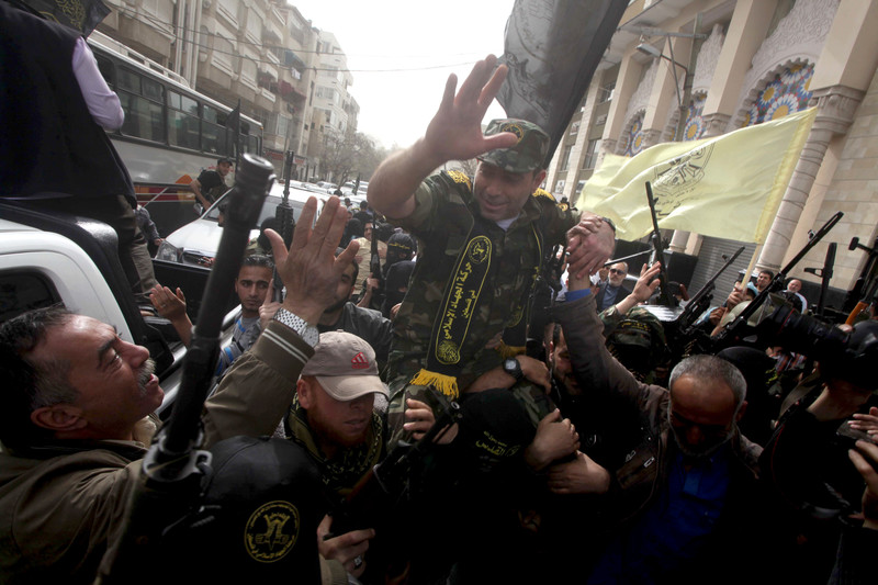 Man wearing military fatigues waves as he is carried by crowd bearing guns and flags