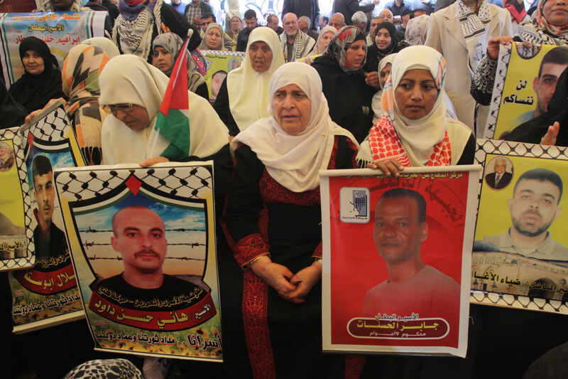 Elderly woman sits amongst crowd holding posters of Palestinian prisoners