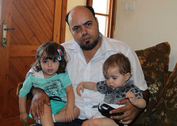 Photo shows Amjad Safadi sitting on couch holding two small girls