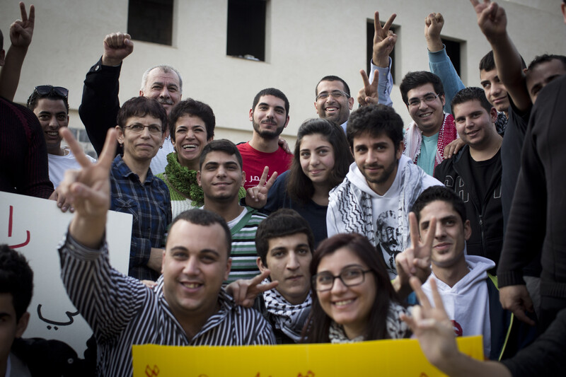 Young man smiles among crowd making victory symbol with their hands