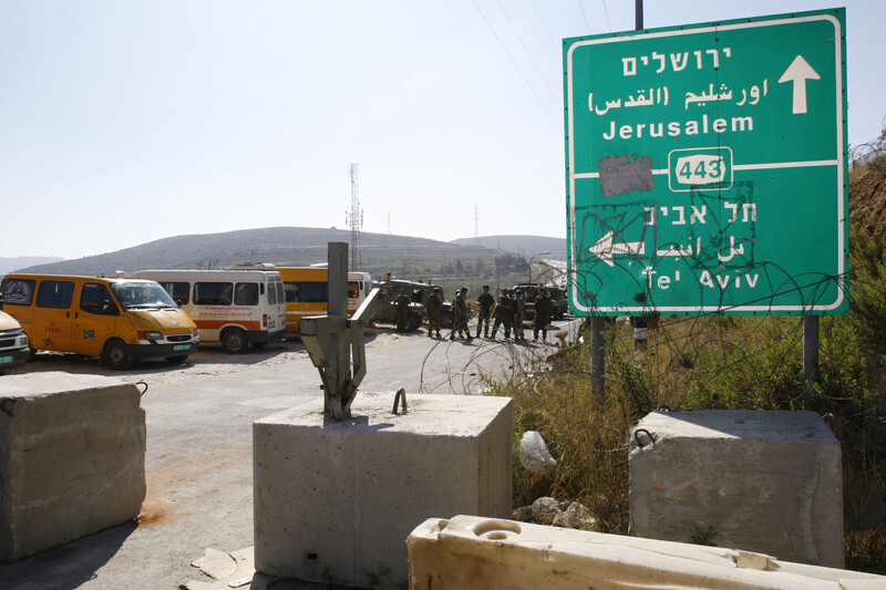 Photo shows highway sign for Route 443 with group of Israeli soldiers forming roadblock in background