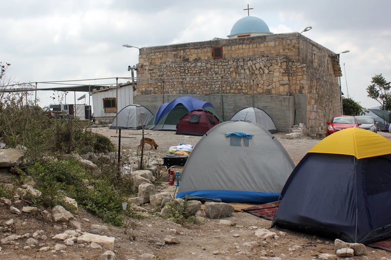 Photograph shows camping tents in front of old church built of stone