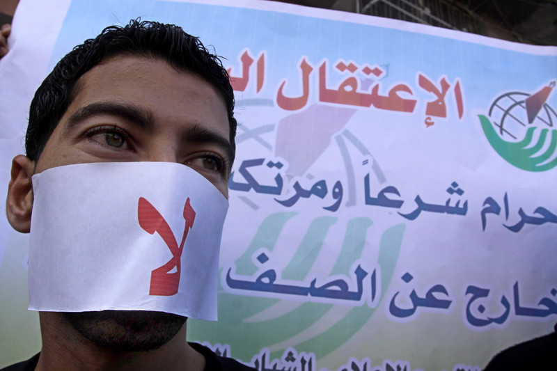 Close-up of man wearing mask over his mouth that says the word no in Arabic in front of press freedom campaign banner