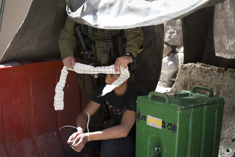 Israeli soldier puts blind fold on zip-cuffed Palestinian youth