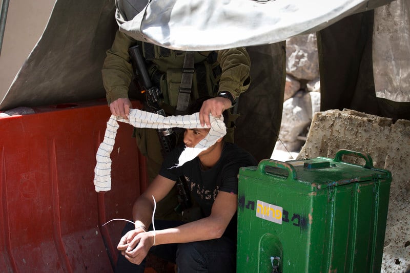 Israeli soldier puts blind fold on zip-cuffed Palestinian youth