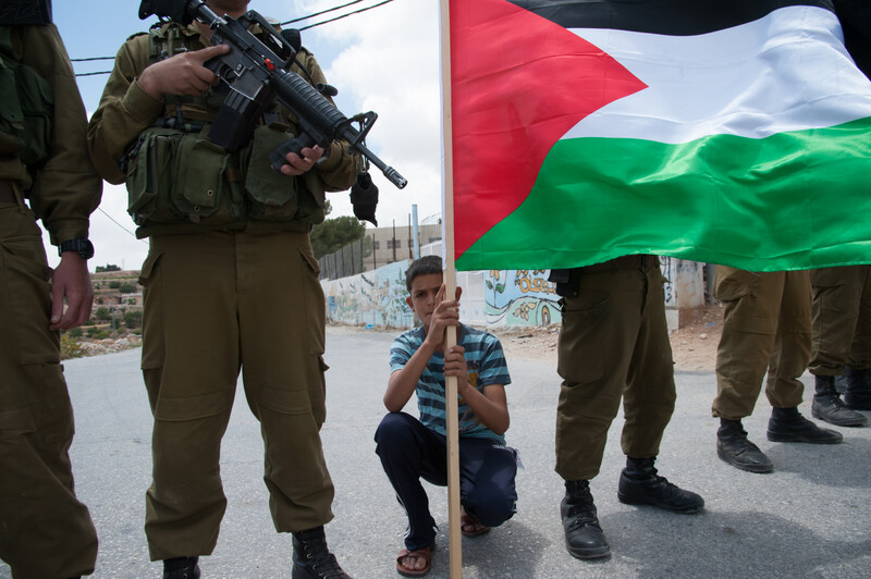 Photo shows boy holding Palestine flag crouching between Israeli soldiers