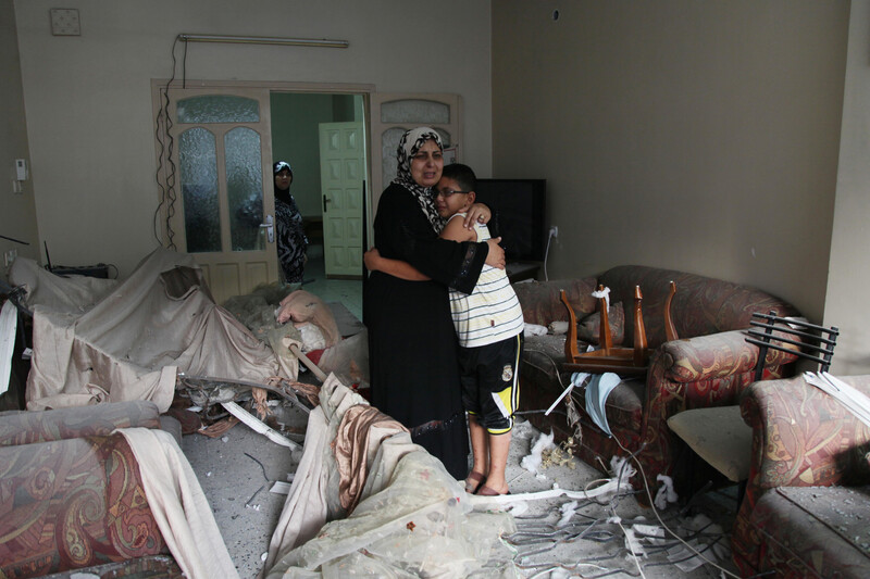 A mother hugs her adolescent son in a bombed-out living room