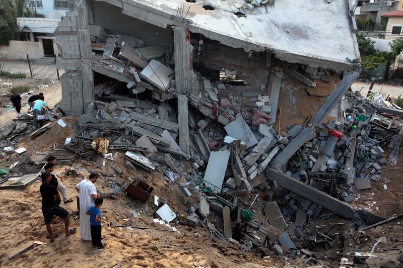 Landscape view of Palestinians observing multi-story residence bombed into a crater