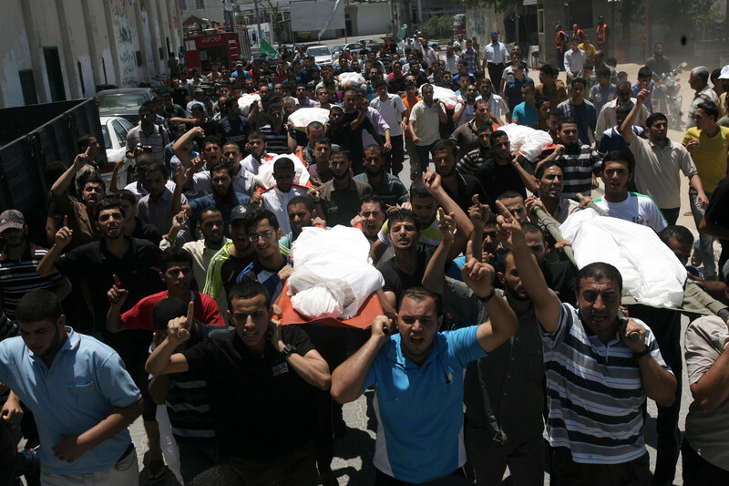 Crowd of men carry shrouded bodies during funeral procession