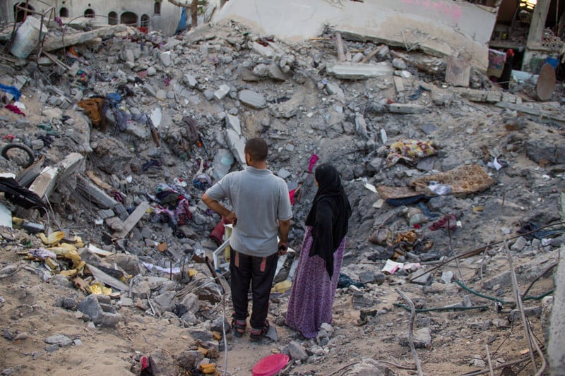 Man and woman look at bombed-out crater where home once stood