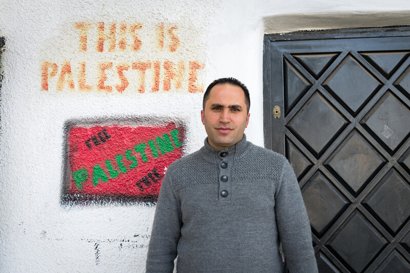 Young man stands in front of wall reading This is Palestine