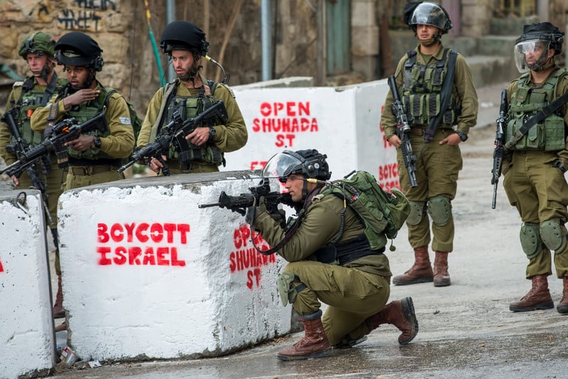 Israeli soldiers carrying arms take position behind concrete blocks reading Boycott Israel Open Shuhada Street