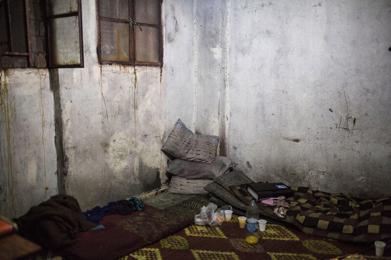 View of corner of room with rust-stained walls and pillows and mats piled on floor