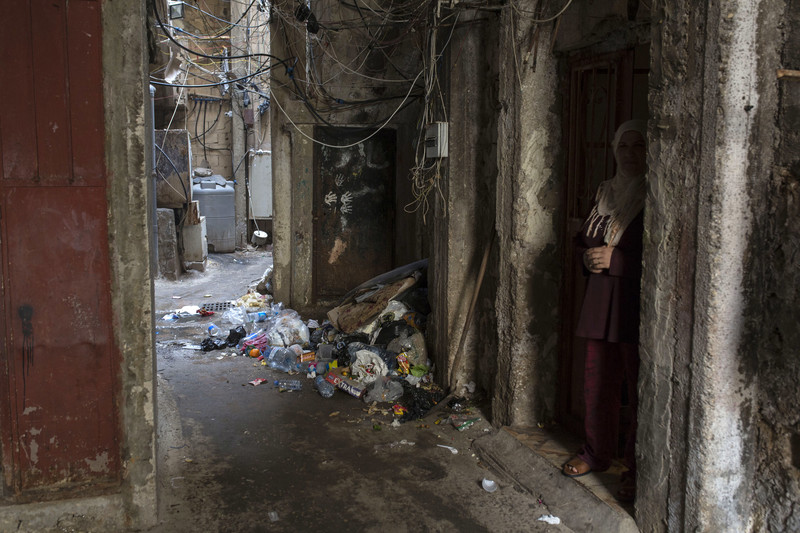Woman stands in doorway in narrow alleyway strewn with trash