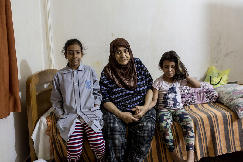 Older woman sits on bed with young girls at either side of her