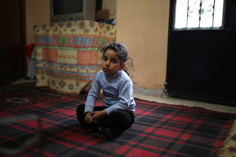 Little girl with a serious facial expression sits on blanket on floor