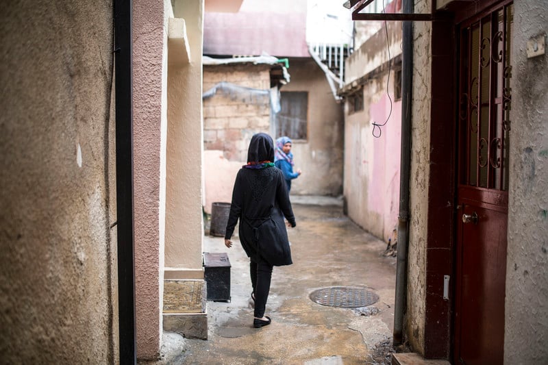 View of young woman's back as she walks in camp alleyway with another woman in front of her