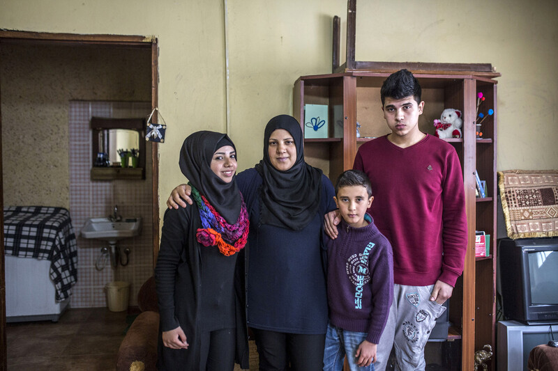 Smiling young woman stands next to woman and two boys in a family room