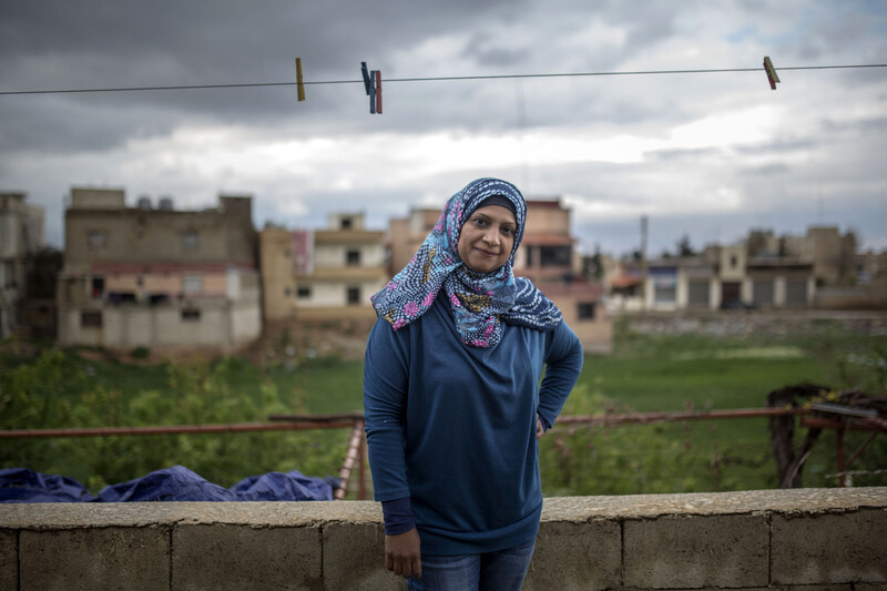 Smiling woman stands underneath clothes line outdoors with buildings and cloudy sky in background