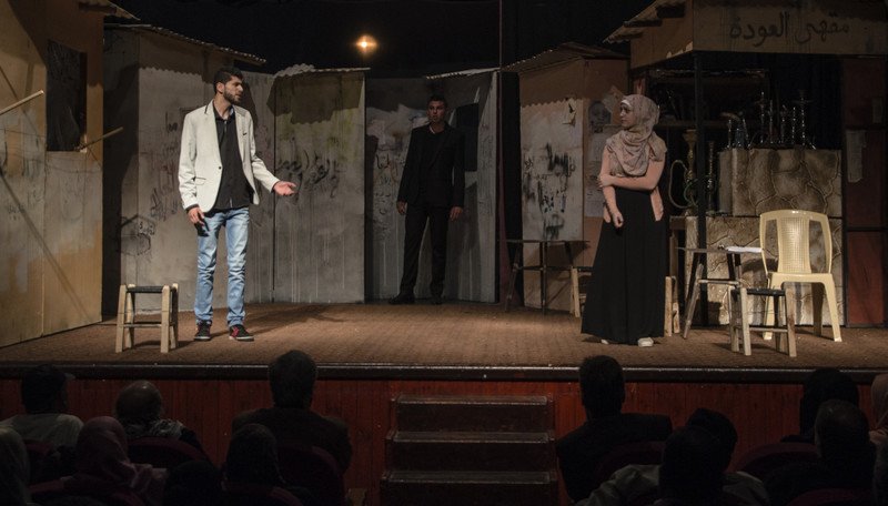 Young man and woman appear on stage as audience sits in foreground