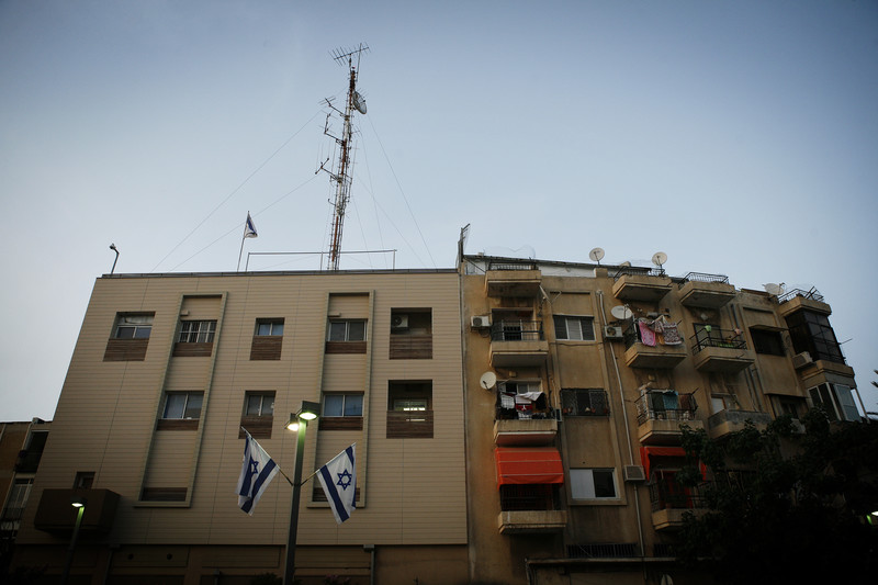 View of plain building with large antenna on top and Israeli flags hanging in front