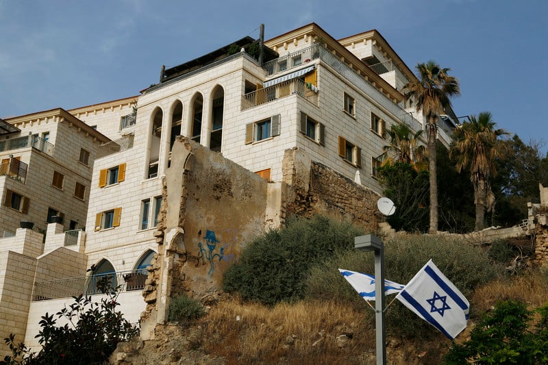 Large luxury building next to old stone wall with Israeli flags hanging in front of it