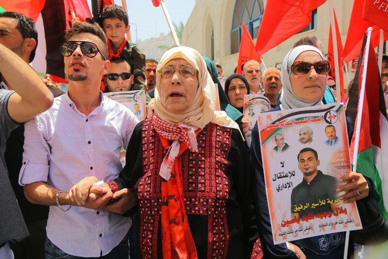 Elderly woman wearing traditional embroidered dress is flanked by two younger relatives at rally