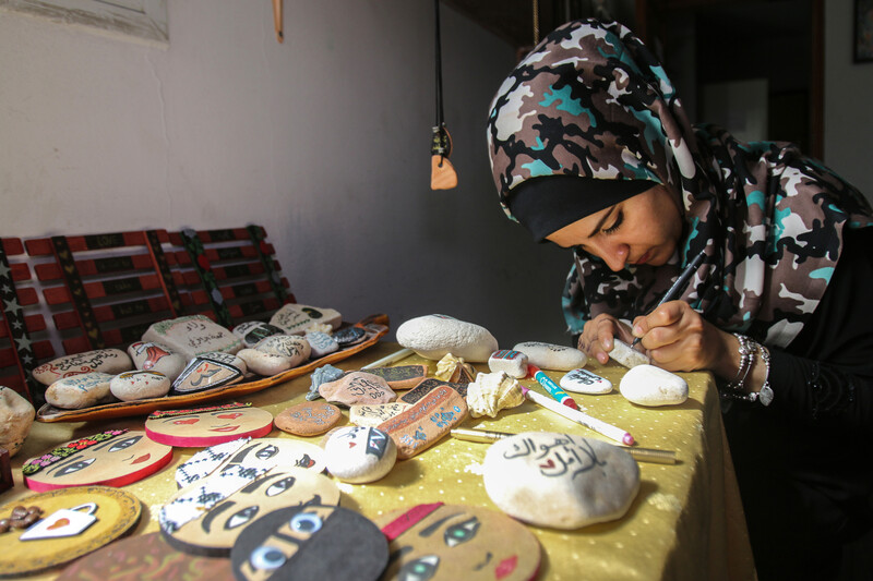 Sitting young woman writes with a pen on a rock while sitting at a table filled with illustrated rocks