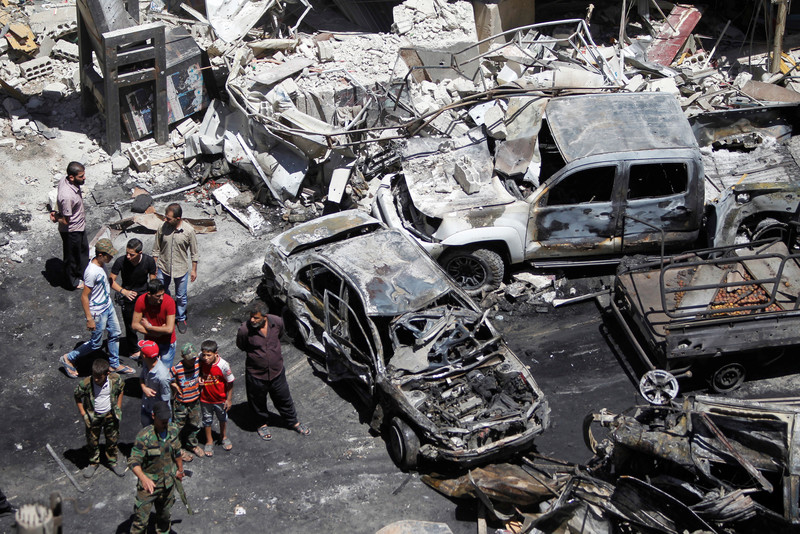 Aerial view of people standing near burnt-out cars and shelled buildings