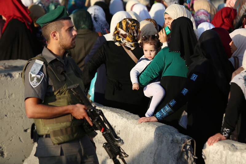 Israeli soldier carrying gun stands in front of queue of women and children at checkpoint