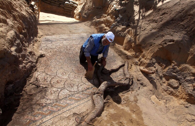 Man wearing baseball cap uses broom to sweep mural featuring a geometric pattern on the ground