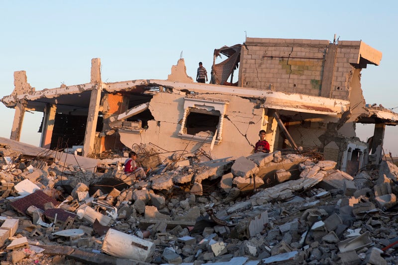 Boys sit on top of rubble in front of destroyed Gaza home