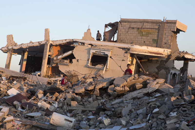 Boys sit on top of rubble in front of destroyed Gaza home