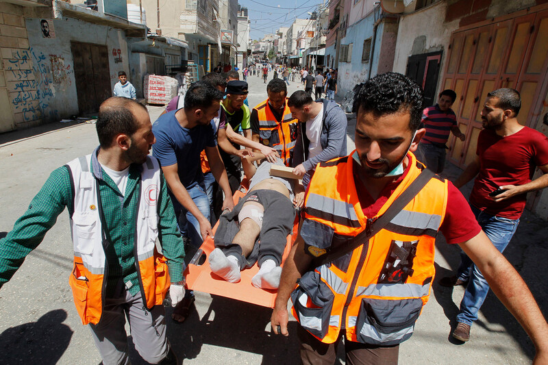 Emergency medics carry man on stretcher with protesters in background