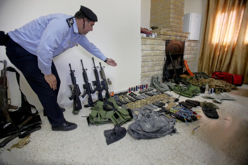Man in uniform gestures towards display of rifles and other weapons