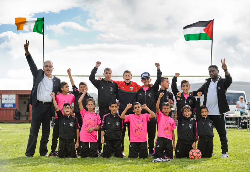 Boys in football jerseys pose with their fists in the air in front of the flags of Ireland and Palestine