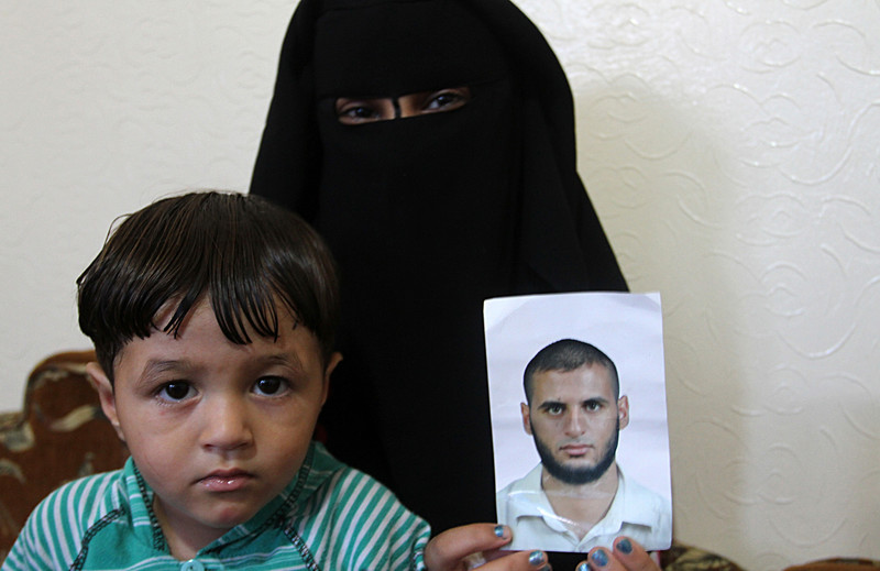 Woman wearing full face covering holds photo of young man as a child sits next to her