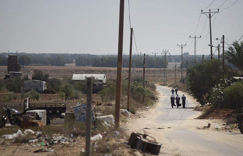 Landscape view of schoolgirls walking along road with Israeli militarized fence in distance