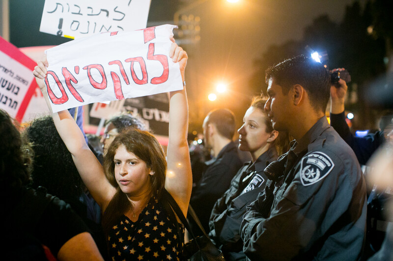 A pair of Israeli police officers, one a woman and the other a man, watch as a protesting woman holds a Hebrew-language sign over her head