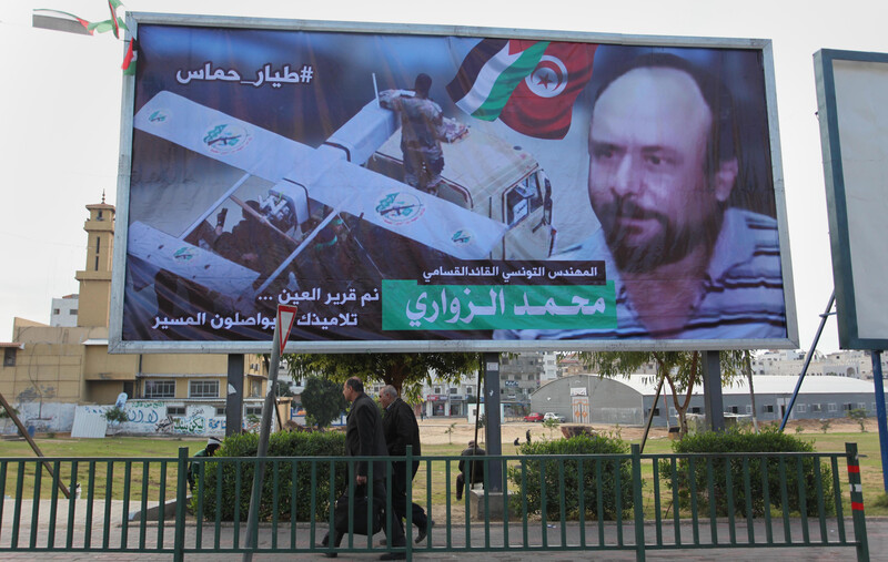 People walk past billboard showing man's face and a drone