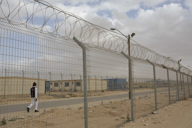 Man walks in between barracks and barbed wire fencing