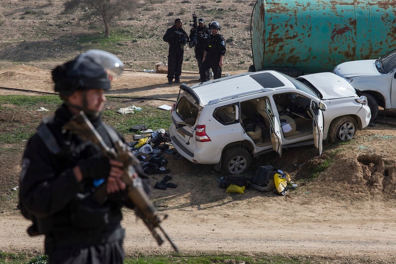 Militarized police officer holding rifle stands in foreground with SUV emptied of its contents in background