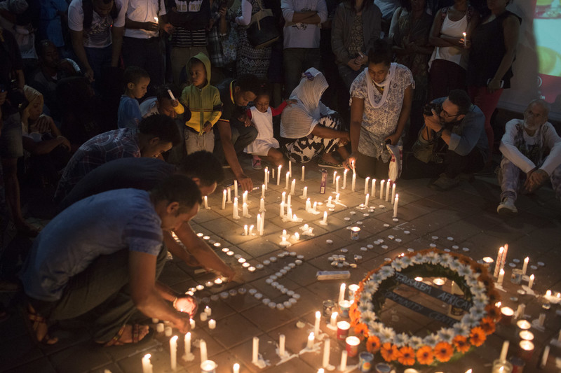 People gather around lit candles, some formed into the shape of a cross