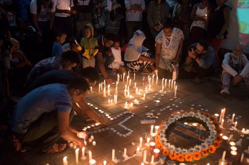 People gather around lit candles, some formed into the shape of a cross