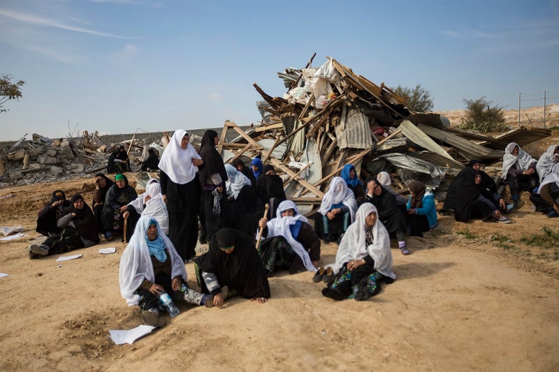 Several women sit in front of pile of debris