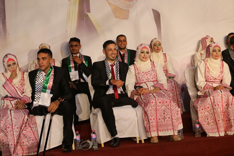 Young women wearing traditional embroidered dresses sit next to young men wearing suits