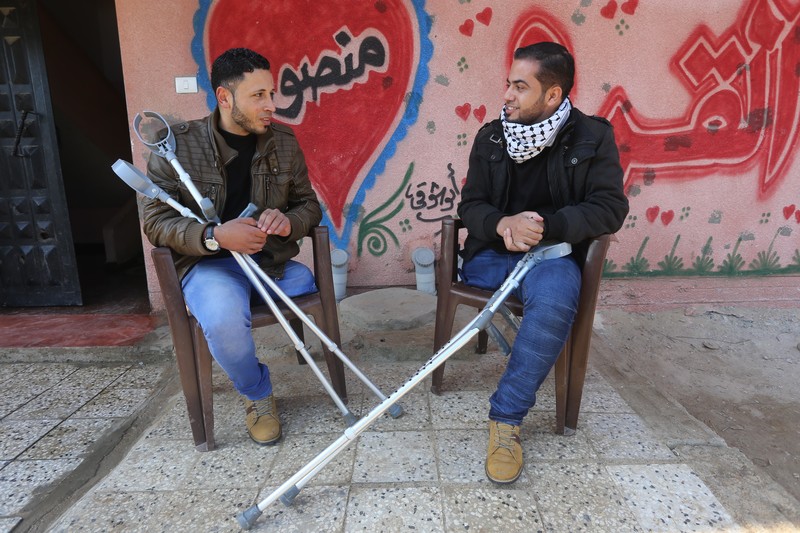 Young men holding crutches sit next to each other, smiling