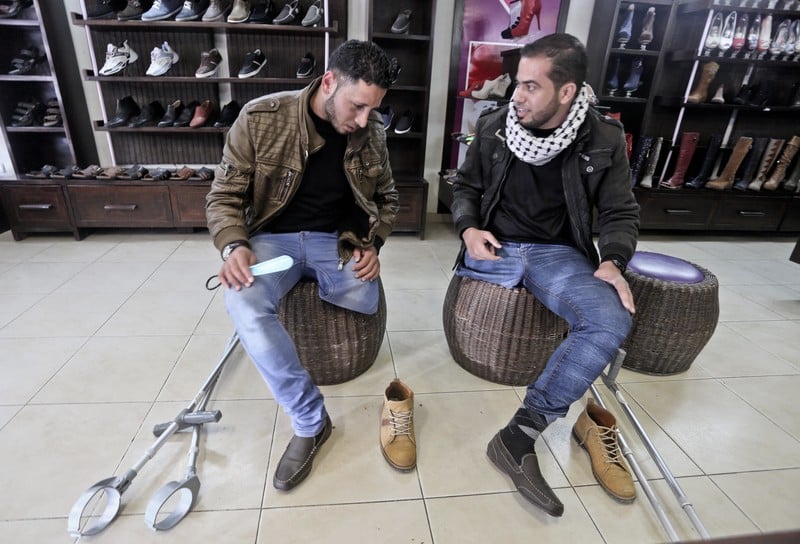 Two young men try on same pair of shoe at store